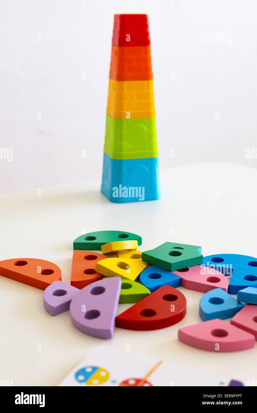 Una torre gradiente di coppette di nidificazione si erge su una parete semplice, mentre sotto di essa si trovano forme di legno assortite. Design semplice e colori felici Foto Stock