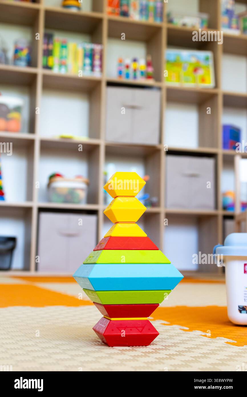 Una scultura geometrica impilabile realizzata con blocchi esagonali colorati si erge su un morbido tappetino con ripiani portaoggetti dietro. La giocosa torre mette in risalto l'equilibrio Foto Stock