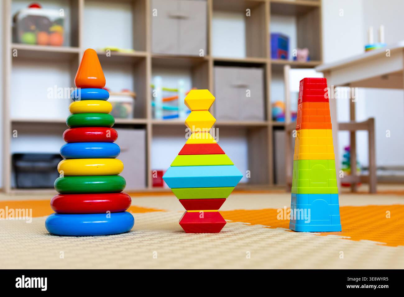 Tre coloratissimi giocattoli impilabili affiancati su blocchi di diamanti e coppette di nidificazione. Una vivace scena in età prescolare Foto Stock