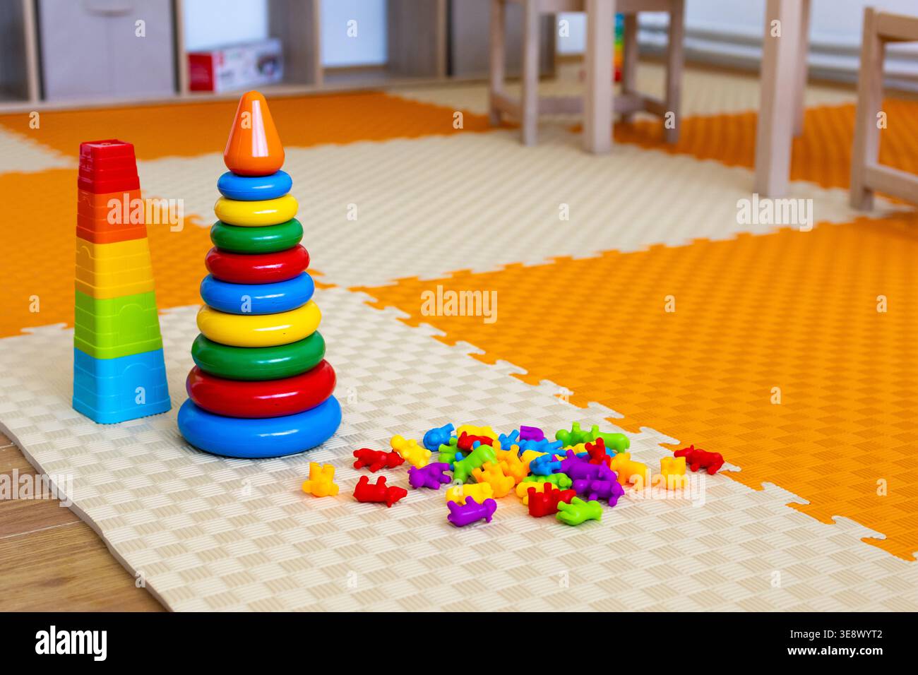 Le tazze impilabili arcobaleno e una grande torre ad anello si trovano su un tappetino in schiuma accanto a una luminosa pila di orsi contatori. Un ambiente allegro per l'infanzia. Foto Stock