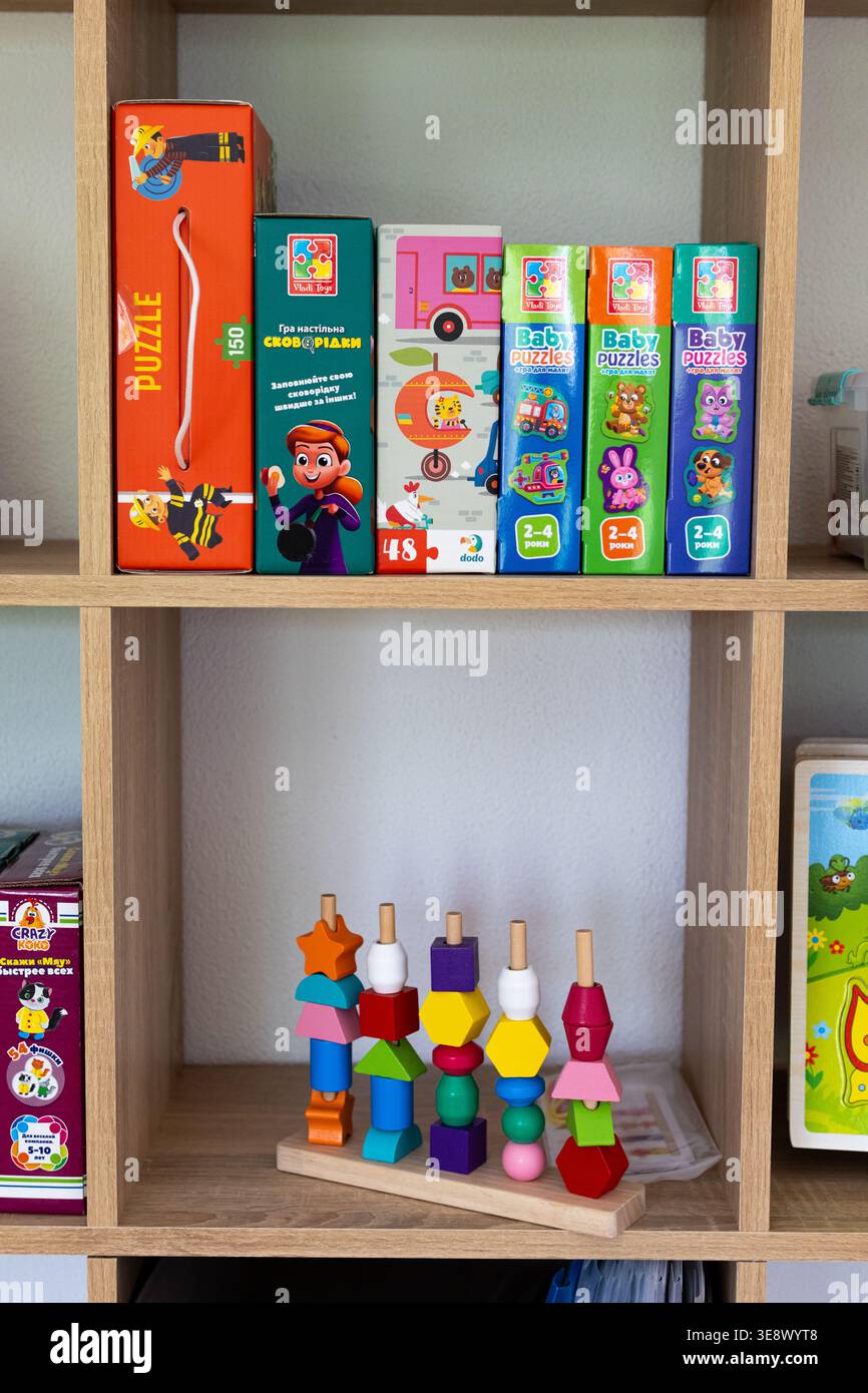 Scaffalature in legno piene di puzzle per bambini e giocattoli educativi in una luminosa sala giochi. Le scatole colorate si abbinano alla parte superiore mentre lo smistatore impilabile Foto Stock