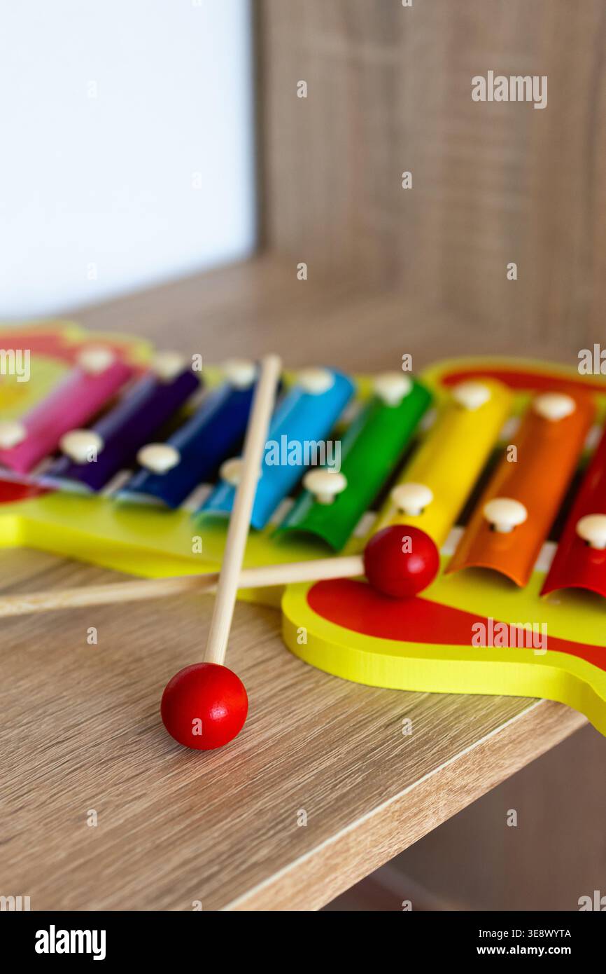 Colorato xilofono giocattolo con mazzuoli rossi appoggiati su una superficie di legno. Le luminose barre in metallo dalle tonalità arcobaleno invitano alla musica allegra Foto Stock