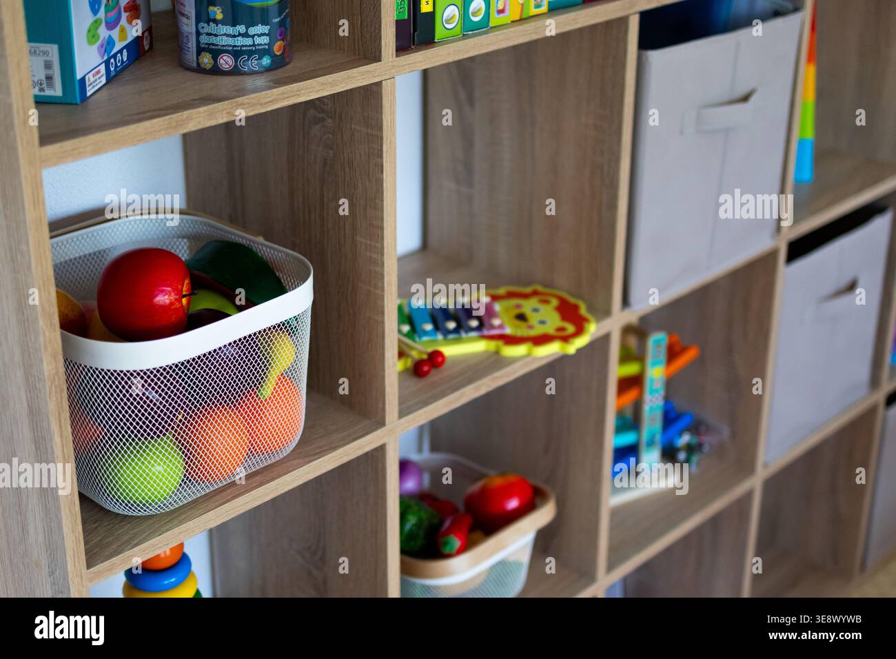 Guarda da vicino i ripiani del vano portaoggetti con un cestino di frutta giocattolo e uno xilofono al leone. L'organizzazione giocosa mostra enigmi e bidoni disposti per un facile accesso Foto Stock