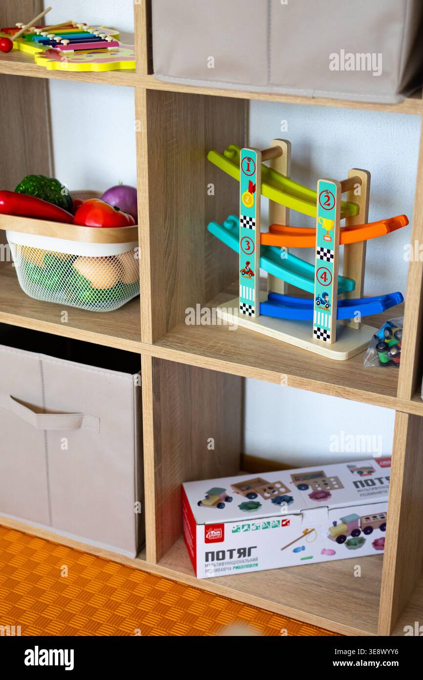 Vano portaoggetti in legno con un giocattolo da corsa a rampa e bidoni morbidi disposti in modo ordinato. Nelle vicinanze ci sono un cestino di cibo finto e uno xilofono leone Foto Stock