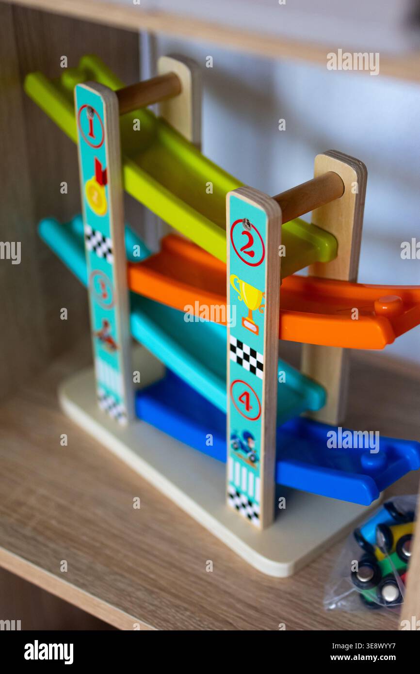 Un colorato giocattolo in legno con quattro piste a zigzag si trova su uno scaffale in una sala giochi. La grafica brillante e le auto da corsa invitano a divertirsi a esplorare Foto Stock