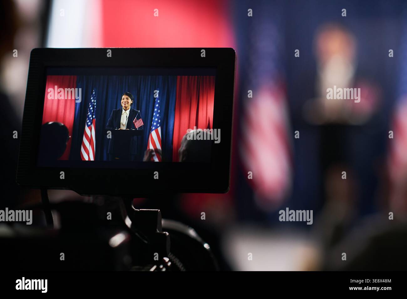 Primo piano del monitor della telecamera che mostra una donna che tiene un discorso politico sul podio con le bandiere degli Stati Uniti. Adatto per campagne elettorali, mezzi di informazione, politica pubblica, uso della comunicazione civica Foto Stock