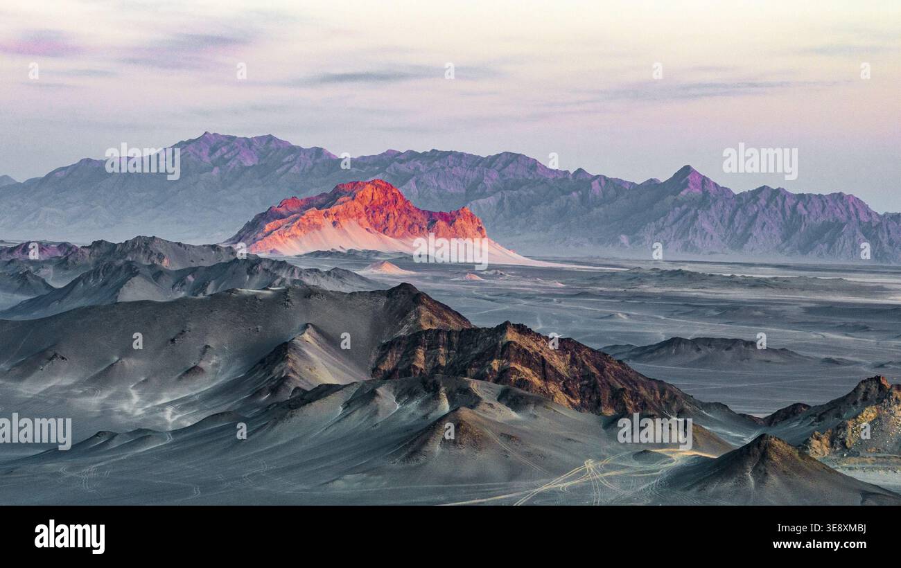 La luce del tramonto illumina il Monte Yanzhi oltre le scure creste del Monte Heidu a Qinghai, Cina. La prospettiva aerea cattura un contrasto straordinario. Foto Stock