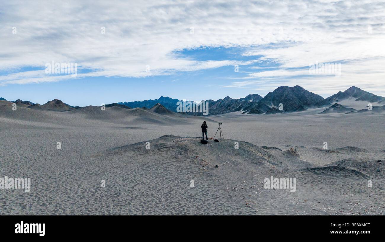 Fotografo solitario in un remoto paesaggio desertico con montagne sullo sfondo, esplorando e fotografando il terreno arido. Foto Stock