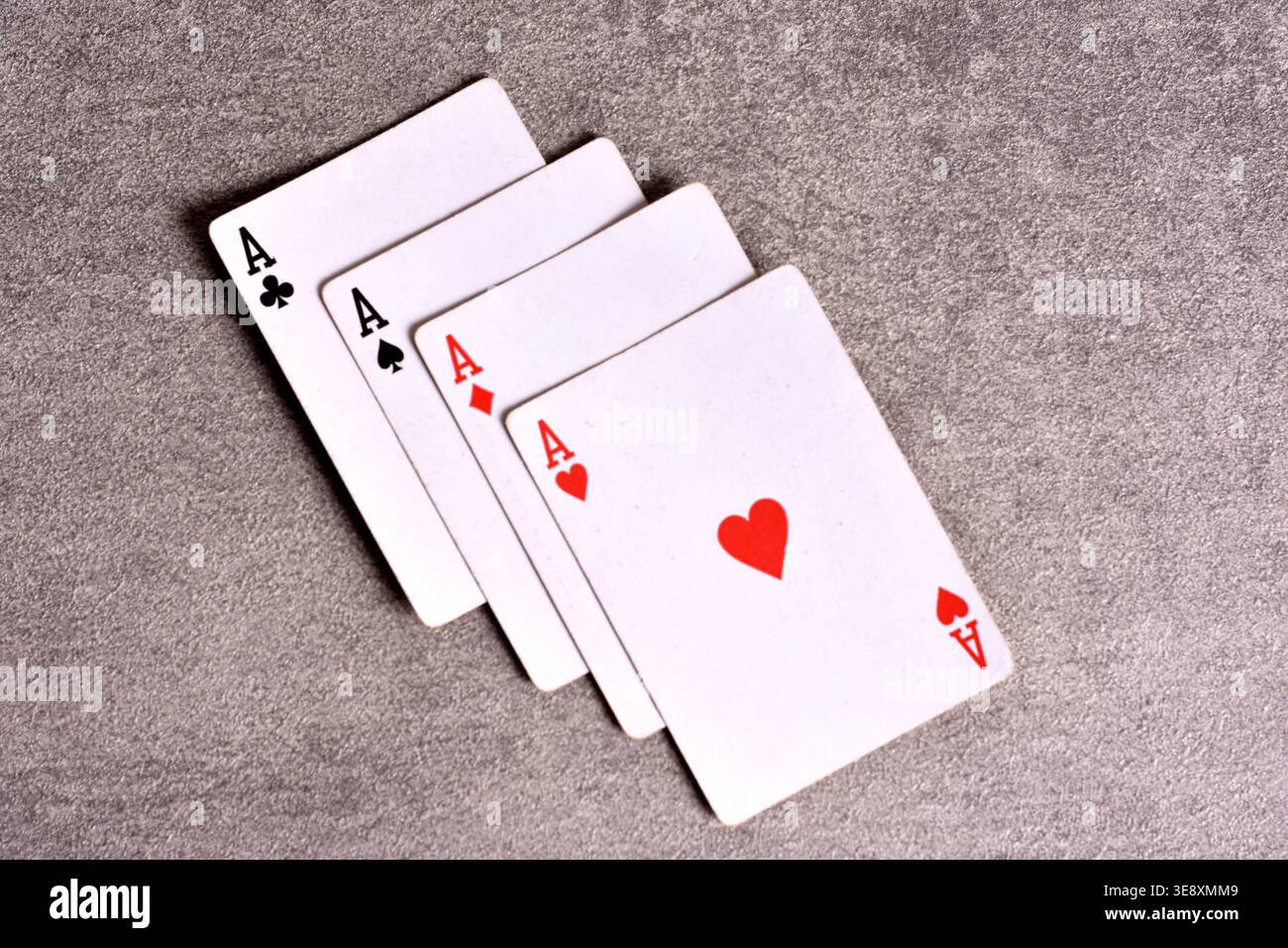 Primo piano ad angolo elevato dei quattro assi da un mazzo standard di carte da gioco, disposte a ventaglio su una superficie grigia in pietra. Foto Stock