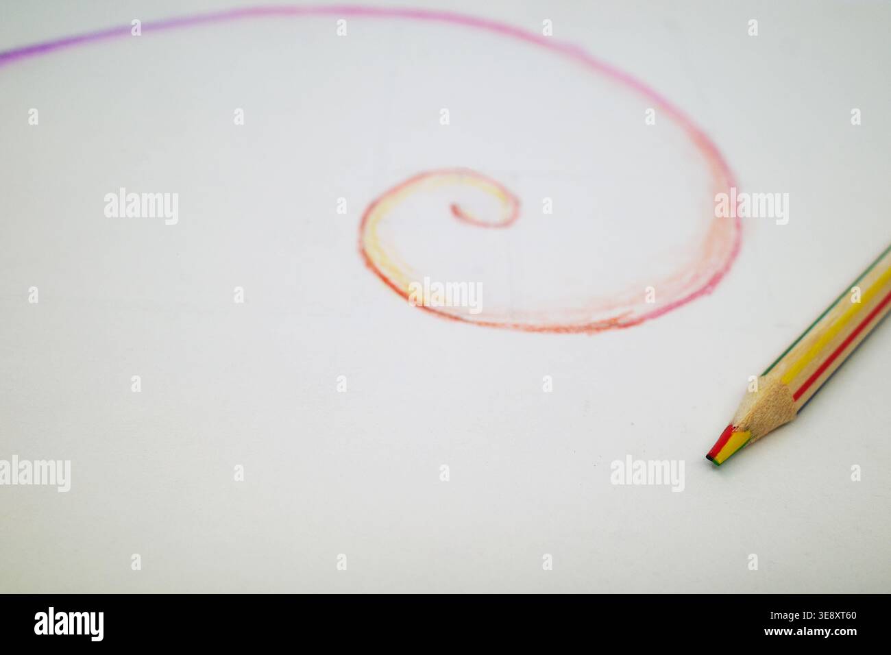 Una matita multicolore poggia su un foglio di carta bianco. Adiacente ad essa si trova una spirale di Fibonacci, che inizia piccola e si espande verso l'esterno in cur liscio Foto Stock