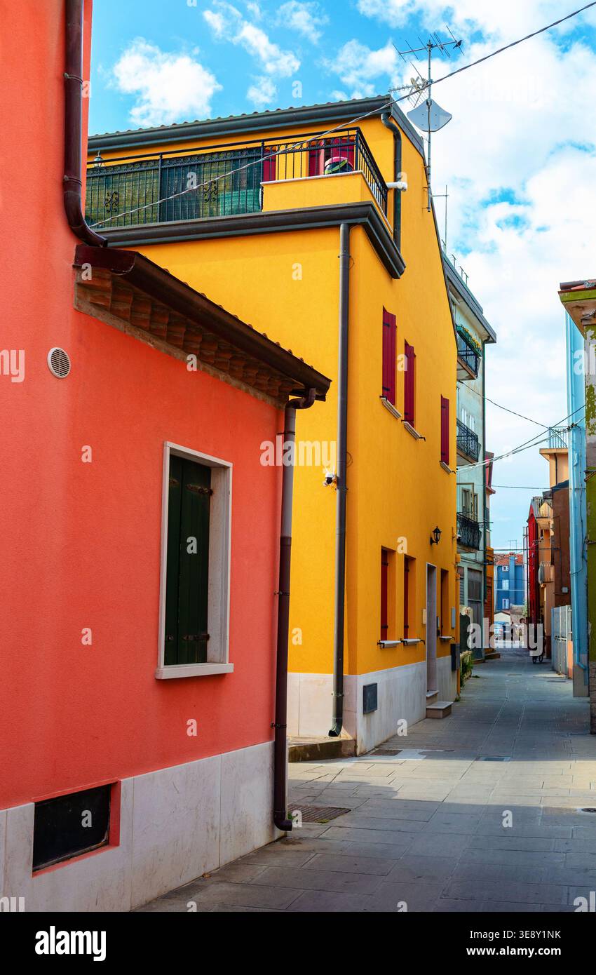 Stradina stretta di Chioggia, Italia, che presenta edifici colorati con facciate arancioni e gialle, creando una pittoresca scena urbana sotto un blu chiaro Foto Stock
