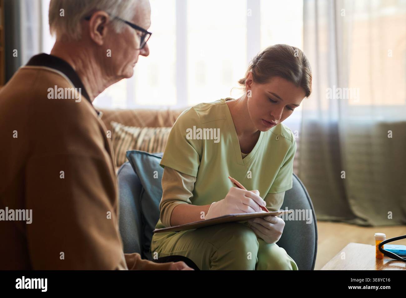 Senior uomo caucasico consulenza giovane adulto caregiver in casa di cura, discutere esigenze di salute mentre caregiver prendere appunti Foto Stock