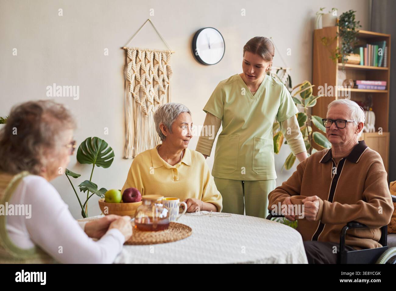 Infermiere senior che assiste i residenti anziani durante il tè nella casa di cura, sostenendo l'assistenza quotidiana e l'interazione sociale Foto Stock