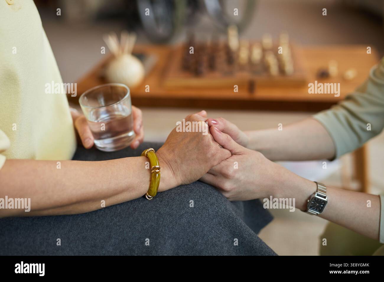 Primo piano di una donna anziana che tiene le mani dell'assistente mentre beve acqua in casa di cura, trasportando supporto e assistenza agli anziani Foto Stock
