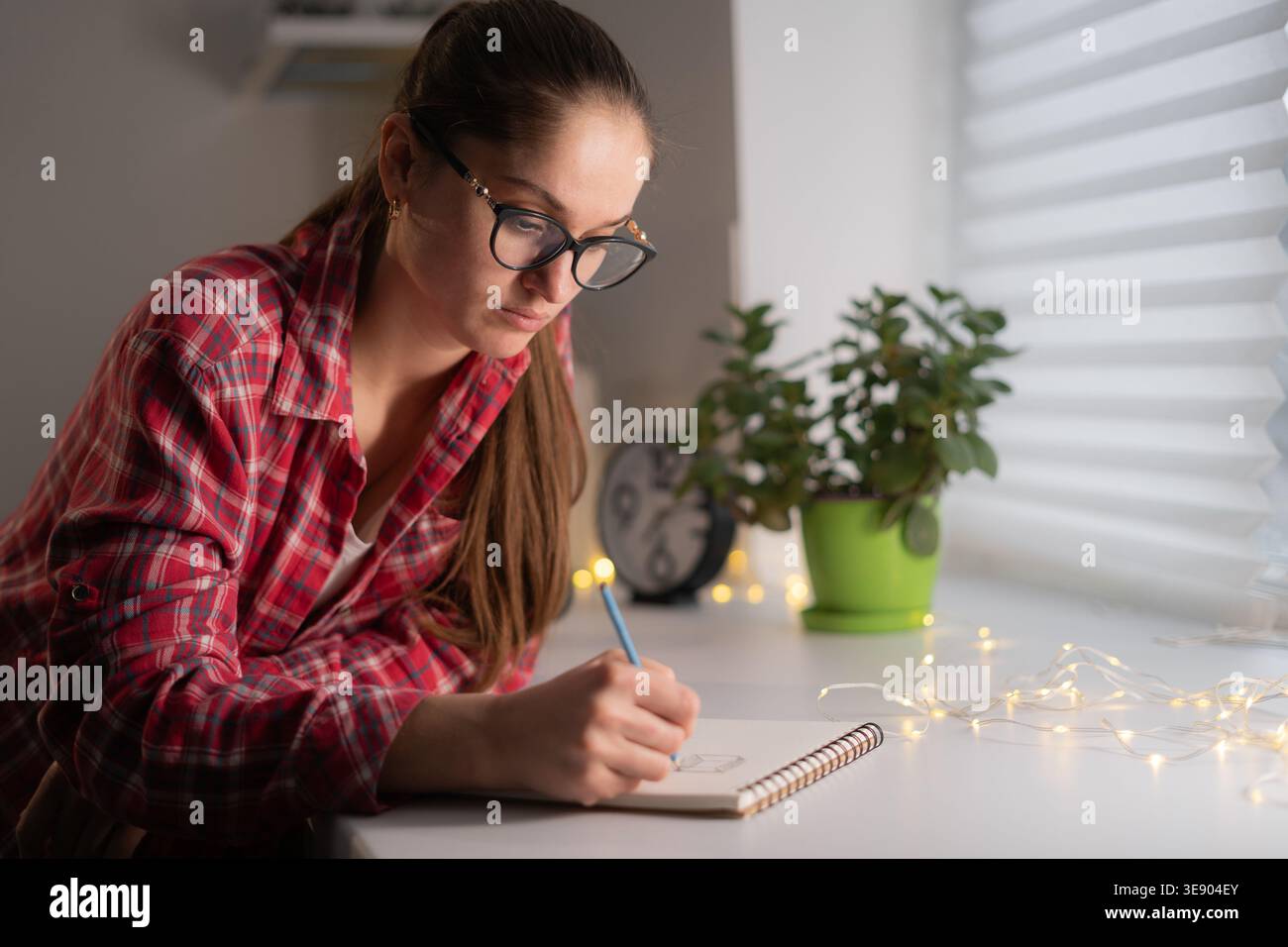 donna in occhiali con appunti a matita sul notebook a casa. diario Foto Stock