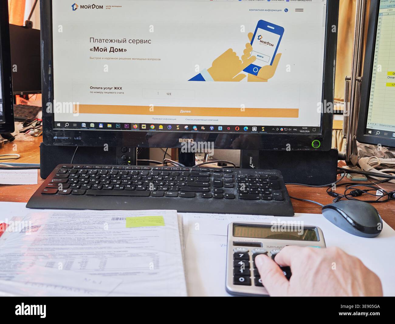 Kirov, Russia - 18 marzo 2026: Una persona lavora sulla pianificazione del budget utilizzando una calcolatrice, documenti finanziari e uno schermo del computer che mostra una paga online Foto Stock