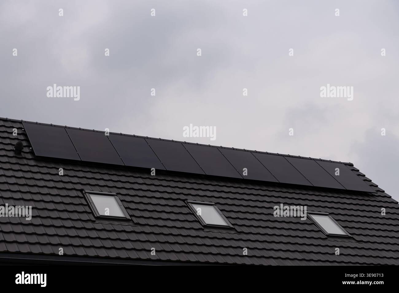 Moderni pannelli solari fotovoltaici installati su un tetto piastrellato scuro di una casa residenziale. Edificio ad alta efficienza energetica con tre finestre attico contro una Foto Stock