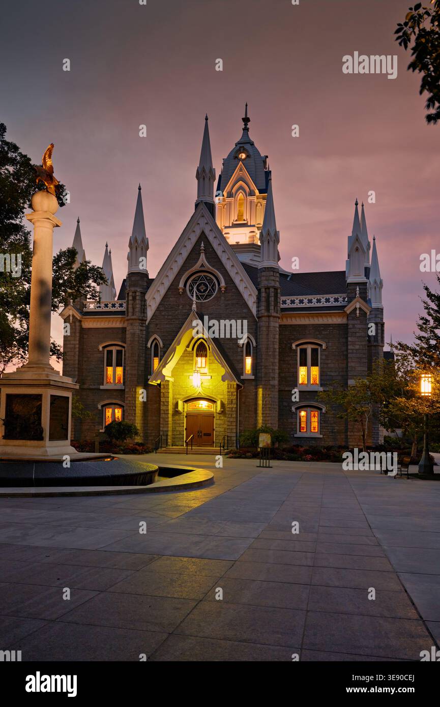 La sala riunioni si trova in Temple Square a Salt Lake City, mentre il sole tramonta. Le luci si illuminano dalle finestre mentre nelle vicinanze si trova un monumento alto. Foto Stock