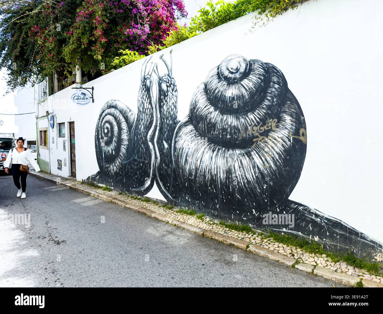 Bianco e nero murale di Street art con due lumache su un muro bianco a Lagos in Portogallo con una donna che cammina sul marciapiede dell'algarve Street art Foto Stock