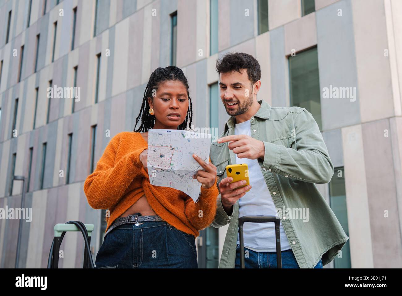 Giovani coppie entusiaste che si impegnano nell'esplorazione mentre consultano una mappa e uno smartphone per navigare attraverso la città, discutendo eccitatamente Foto Stock