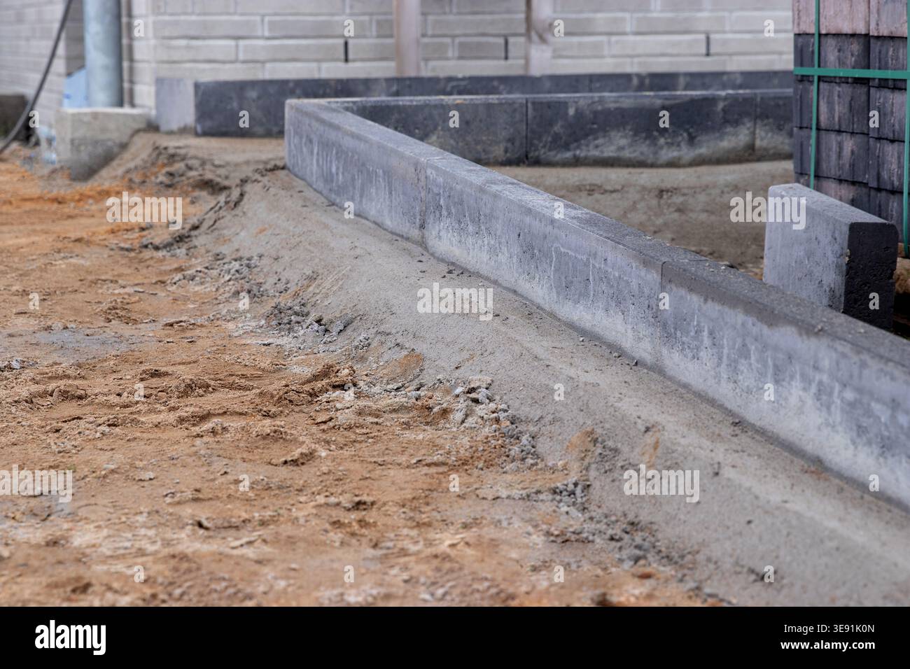 Cantiere che mostra un marciapiede di cemento lungo un percorso sterrato con un muro parzialmente costruito e materiali da costruzione sullo sfondo Foto Stock