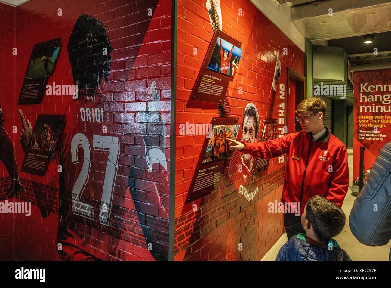 La guida turistica dello stadio LFC conduce un gruppo attraverso il moderno atrio dello Stand principale presso l'Anfield Stadium, evidenziando murales di grandi dimensioni. Foto Stock