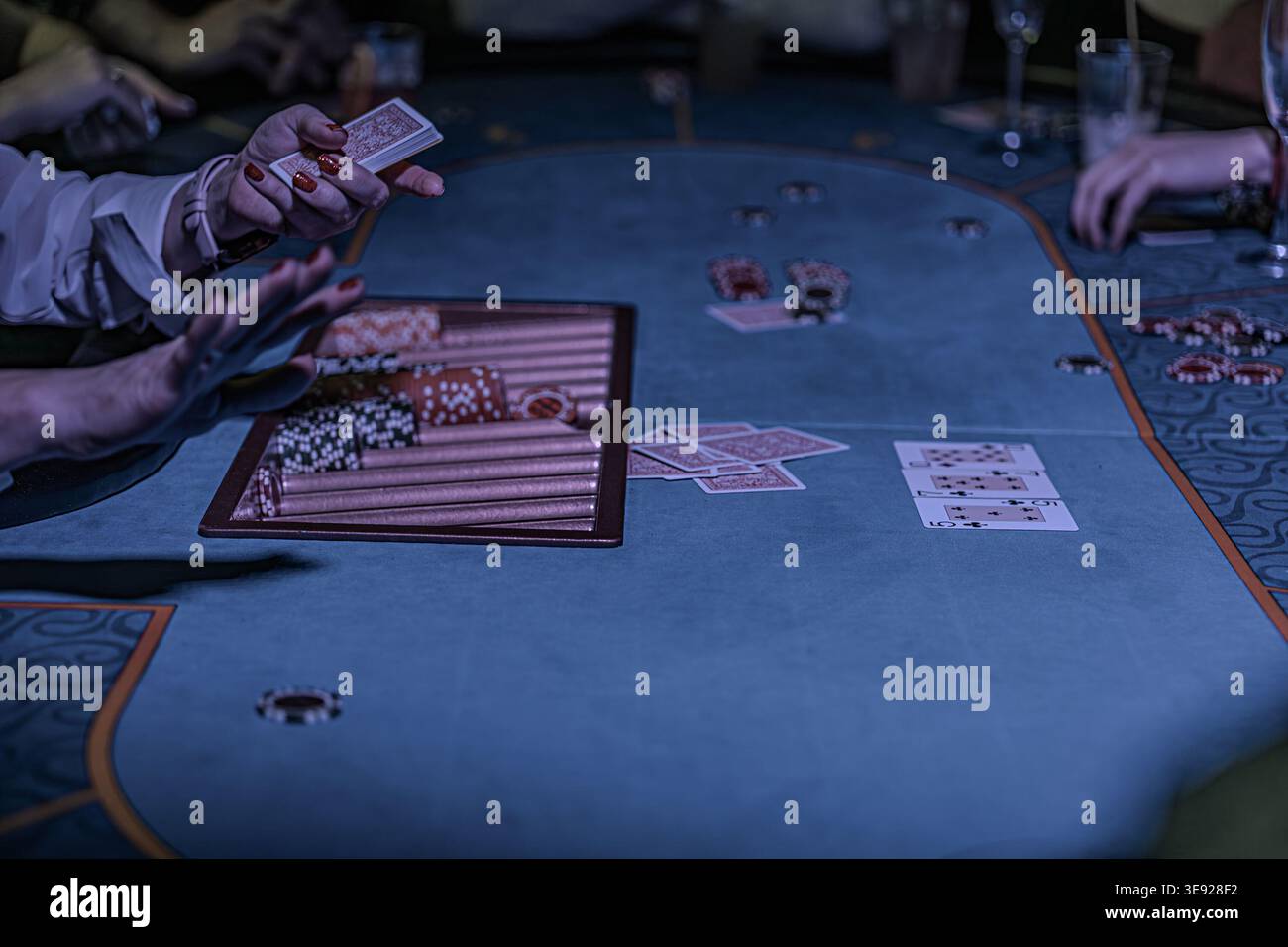 All'interno del vivace casinò Texas Hold Em Game in corso su un tavolo ovale e feltrato di blu tre persone hanno coinvolto carte spacciate di colori diversi Foto Stock