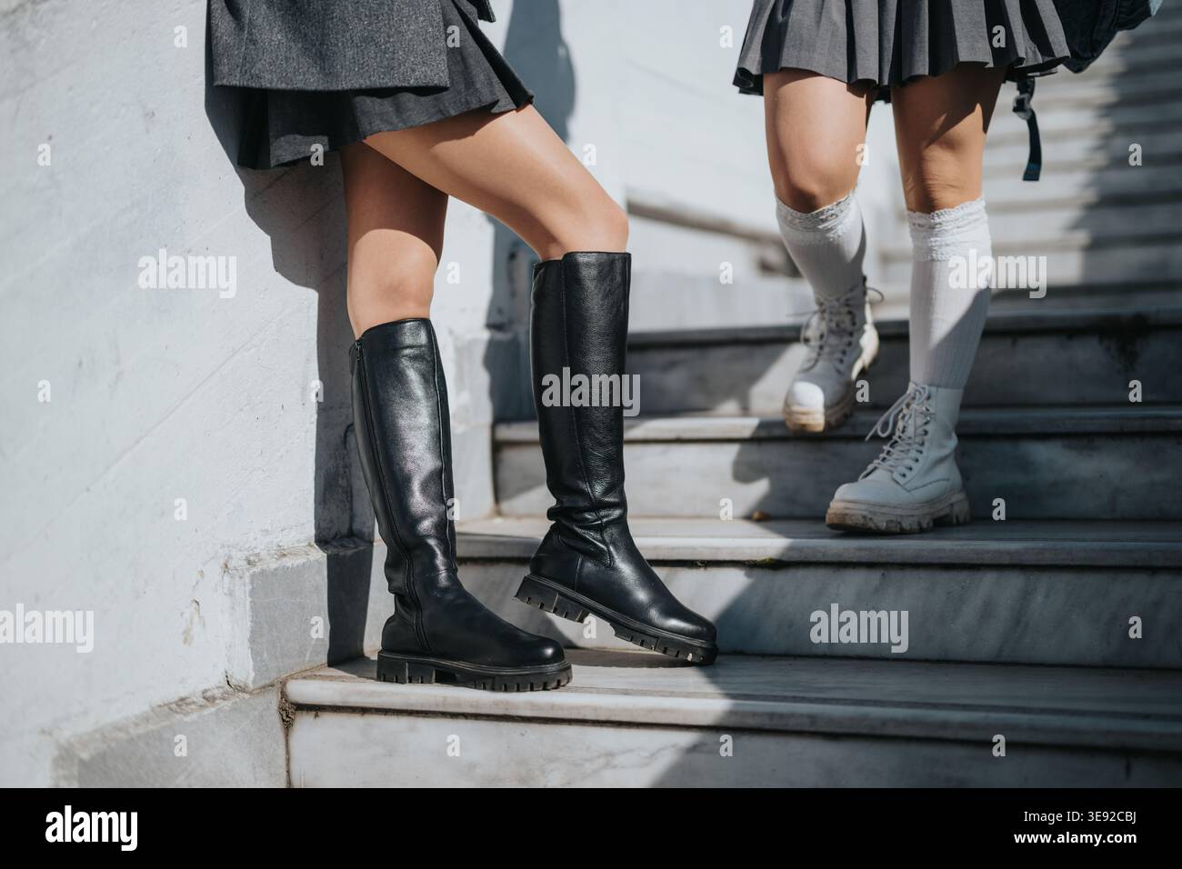 Studenti in gonne scolastiche e stivali in piedi su scale di marmo alla luce del sole Foto Stock