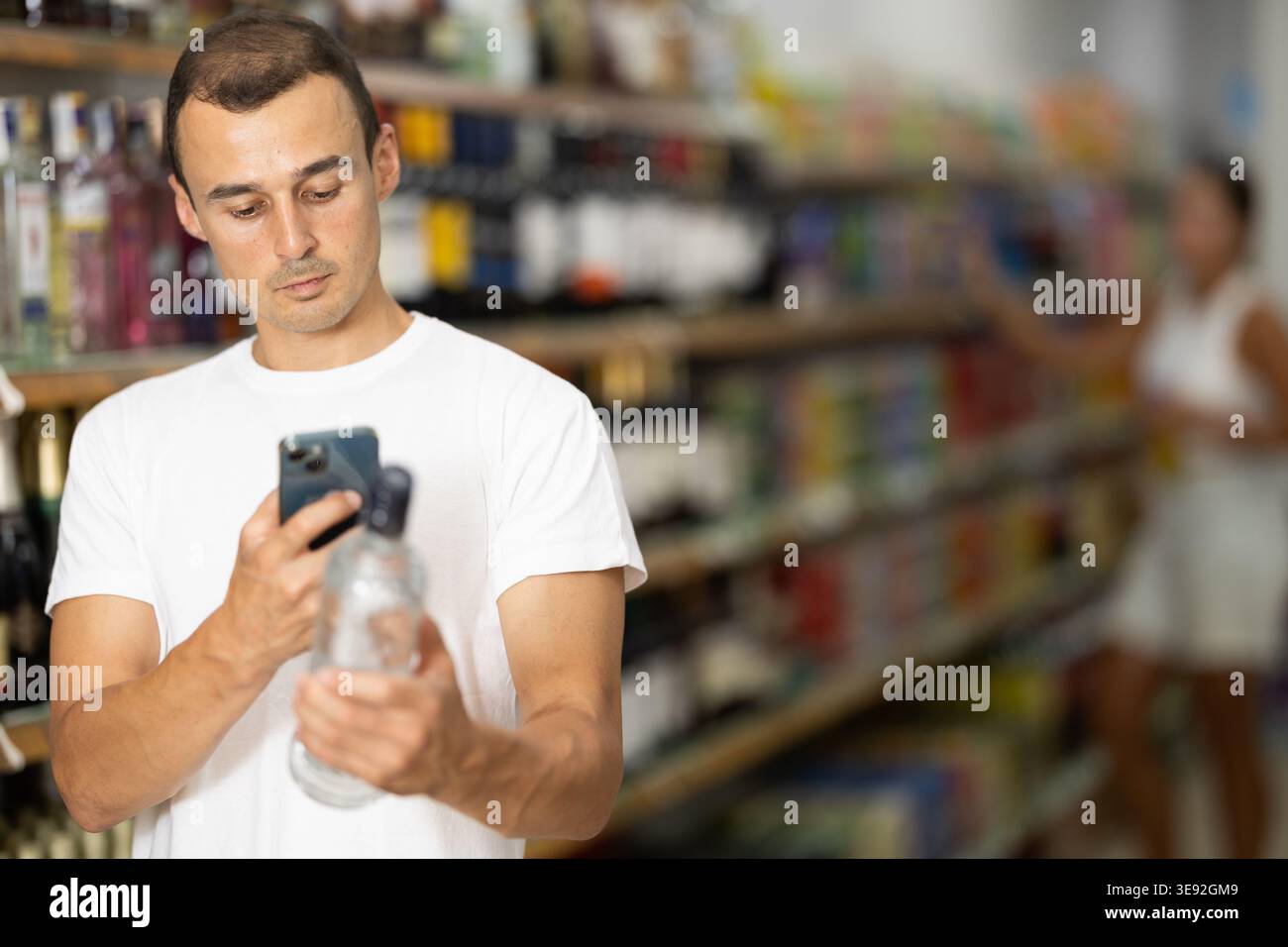 Uomo che utilizza smartphone per la scansione di codici a barre su bottiglie di bevande alcoliche Foto Stock