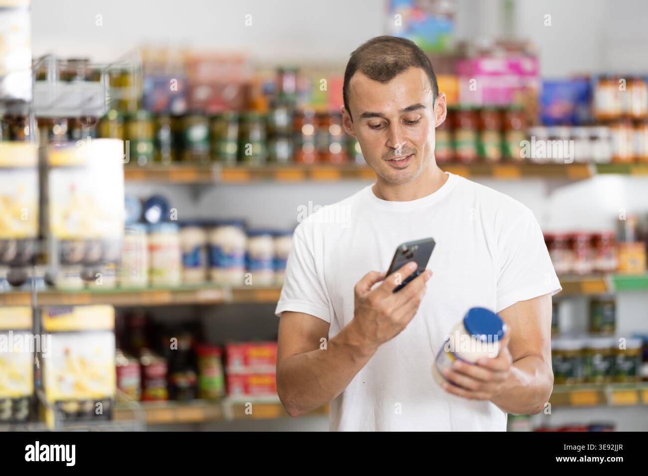 Acquirente maschio che esegue la scansione di codici a barre o codici qr con smartphone su etichetta maionese Foto Stock