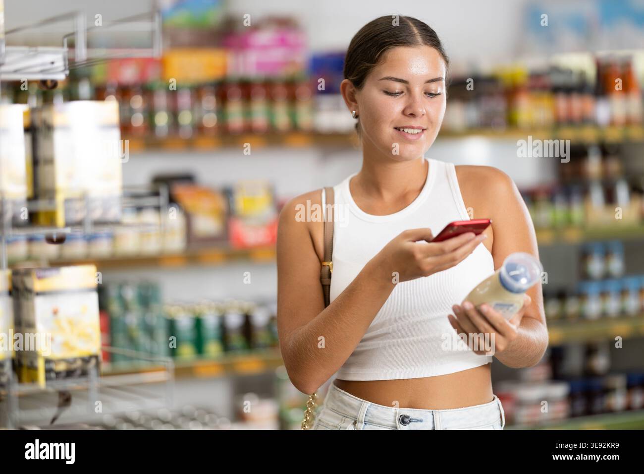 Ragazza che esegue la scansione del codice a barre o del codice qr con lo smartphone sull'etichetta maionese nel supermercato Foto Stock