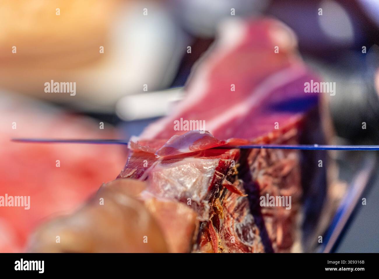 Affettare a mano sottili pezzi di prosciutto. Una visione ravvicinata del prosciutto curato in preparazione al consumo Foto Stock