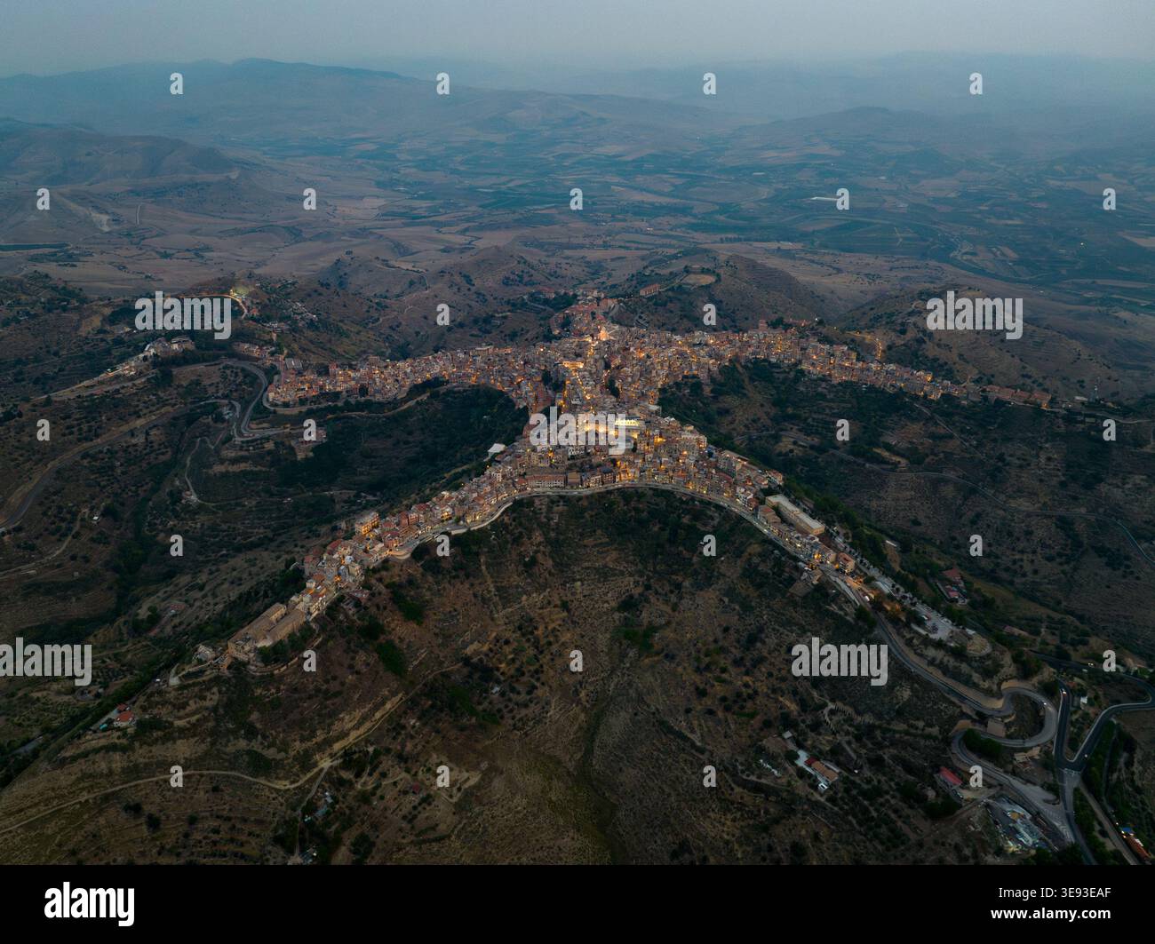 Veduta aerea della storica cittadina di Centuripe con la sua unica forma umana illuminata al crepuscolo tra le dolci colline del paesaggio siciliano Foto Stock