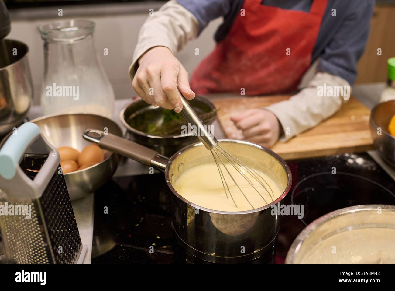 Bambino che mescola la salsa in pentola mentre cucina in cucina, imparando le capacità di preparazione del cibo e l'indipendenza. Utile per la genitorialità, lo stile di vita familiare, il marketing educativo culinario Foto Stock