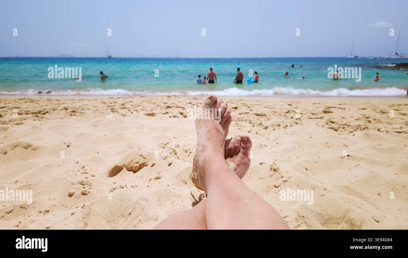 Persona che si rilassa sulla spiaggia, piedi sepolti nella sabbia Foto Stock