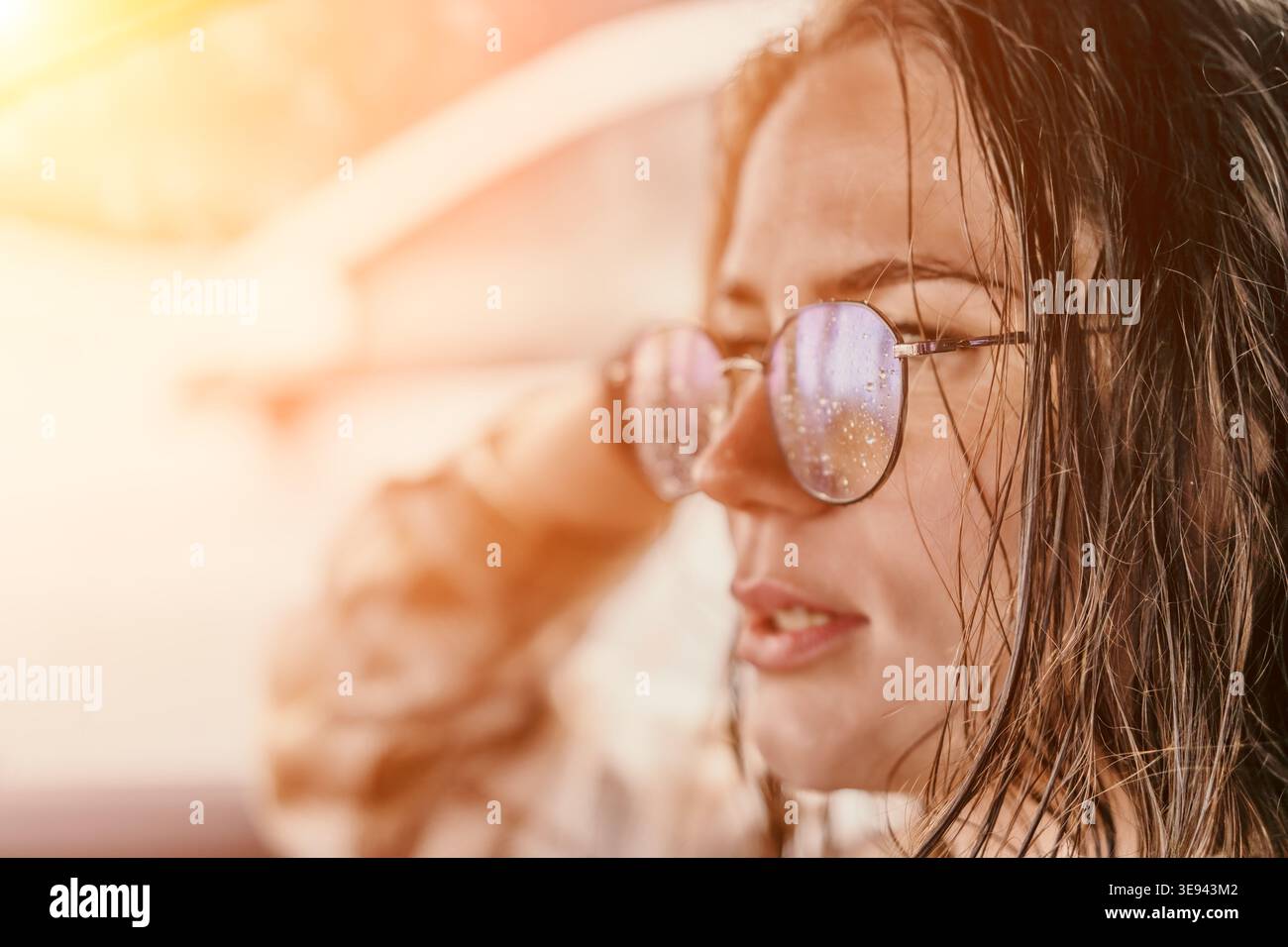 Occhiali da donna giovane donna con capelli bagnati che indossa occhiali ricoperti di gocce d'acqua che guardano lontano durante l'ora d'oro Foto Stock