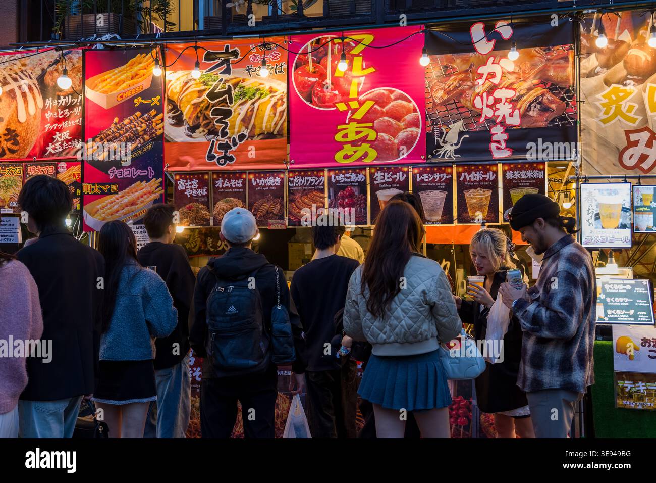 Folle di persone che acquistano spuntini da un colorato stand gastronomico di Tokyo di notte Foto Stock