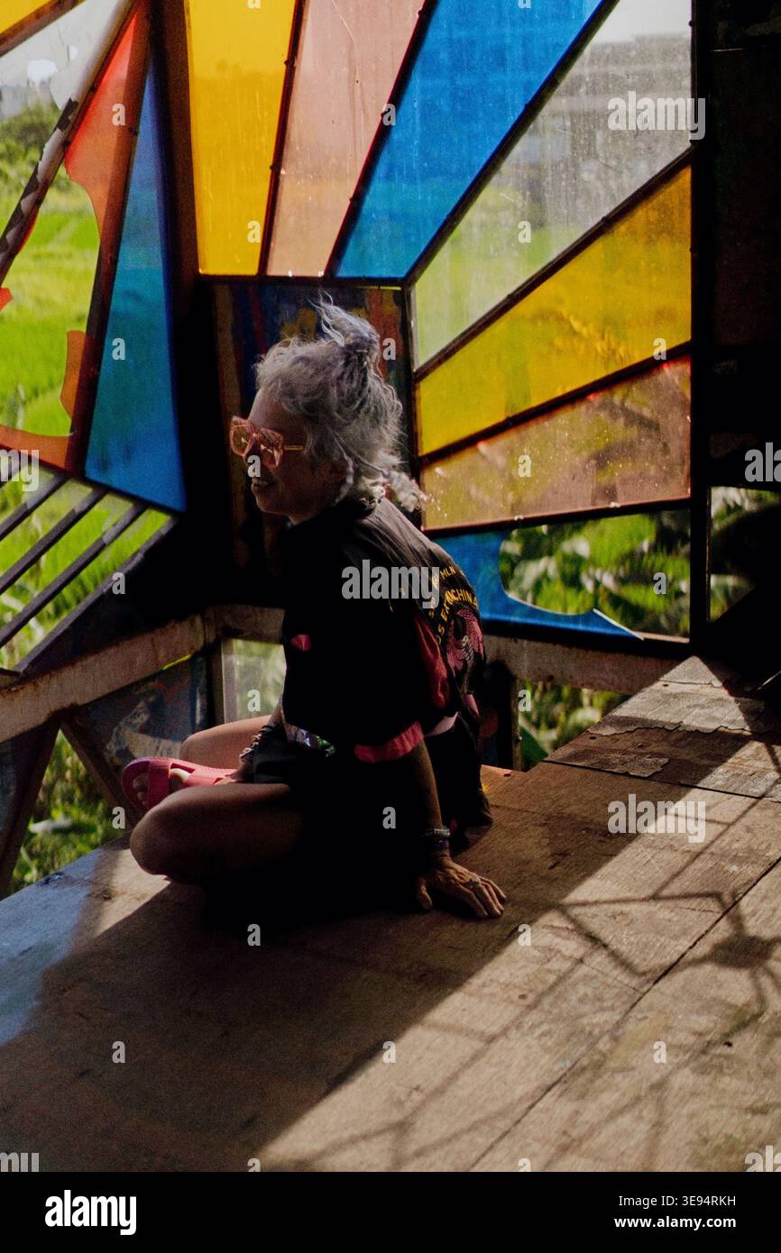 Donna matura seduta a gambe incrociate nel padiglione in vetro colorato di Bali Foto Stock