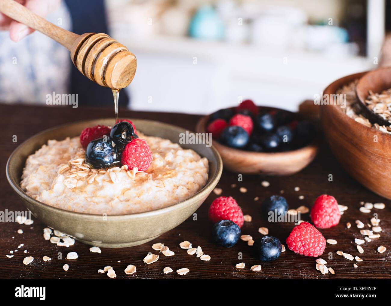 Ciotola per la colazione con farinata d'avena di frutti di bosco, miele sgocciolato in una cucina rustica Foto Stock
