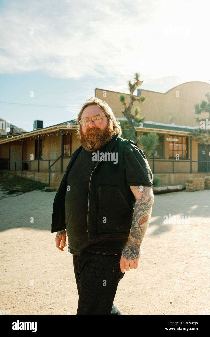 uomo con barba allo zenzero e tatuaggi che cammina accanto a un saloon Foto Stock