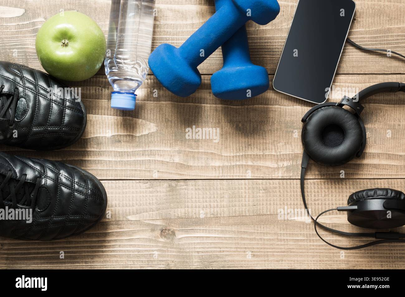 Sport e fitness equipmen con le scarpe da ginnastica, manubri, asciugamano e cuffie sul pannello di legno. Vista da sopra con lo spazio per il tuo testo. Foto Stock