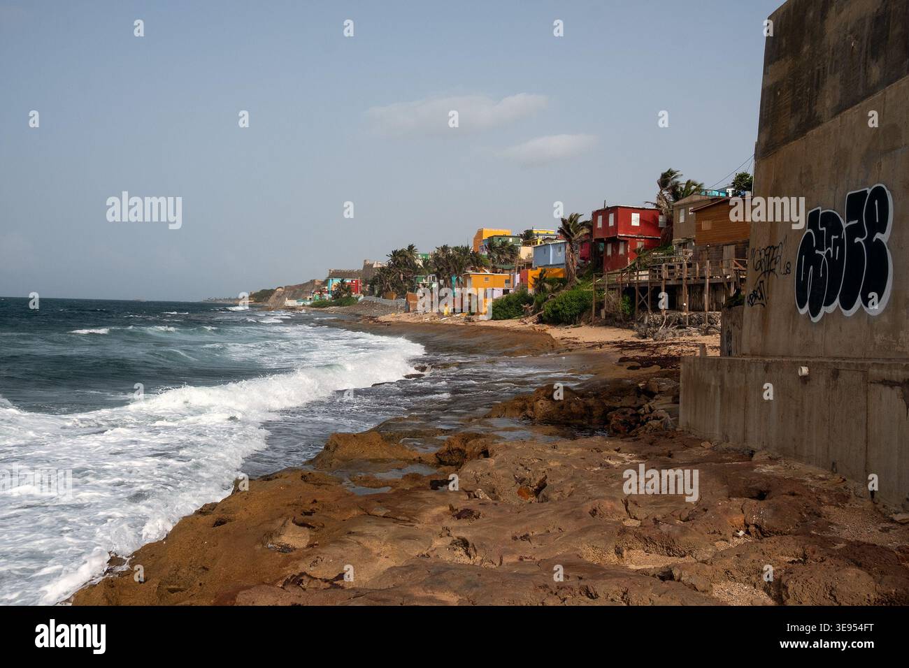 Le onde dell'oceano si infrangono contro una costa rocciosa dove edifici colorati fiancheggiano la spiaggia. Foto Stock