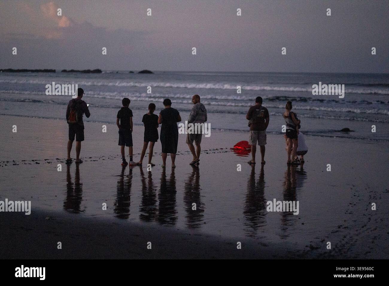 Un gruppo di persone si trova su una spiaggia bagnata al crepuscolo, i cui riflessi sono visibili sulla sabbia. Foto Stock
