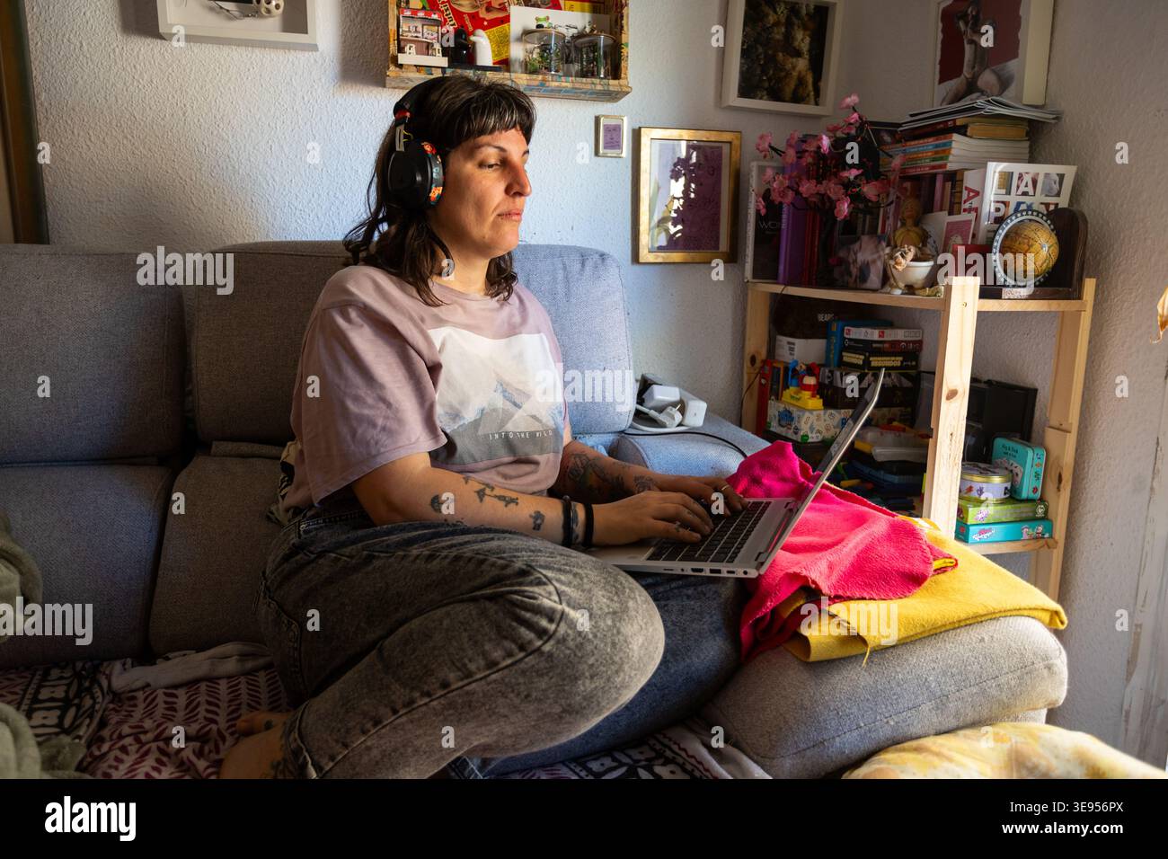 Giovane donna dallo stile indie alternativo che lavora con un notebook a casa per un autentico lavoro da remoto e uno stile di vita libero creativo con tatuaggi e pierci Foto Stock