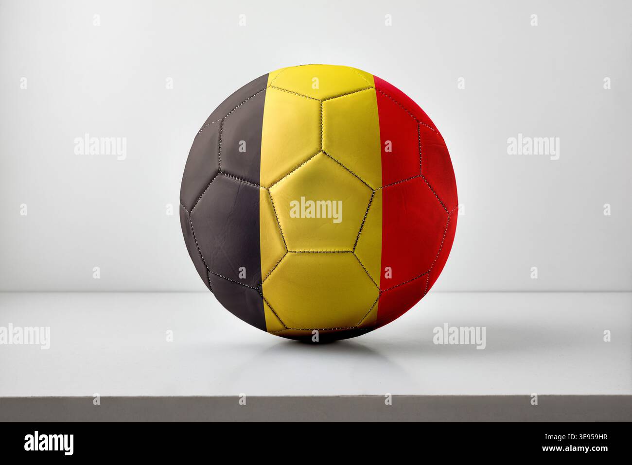 Un pallone da calcio con strisce verticali nere, gialle e rosse del Belgio, centrate su uno sfondo neutro con illuminazione soffusa. Foto Stock