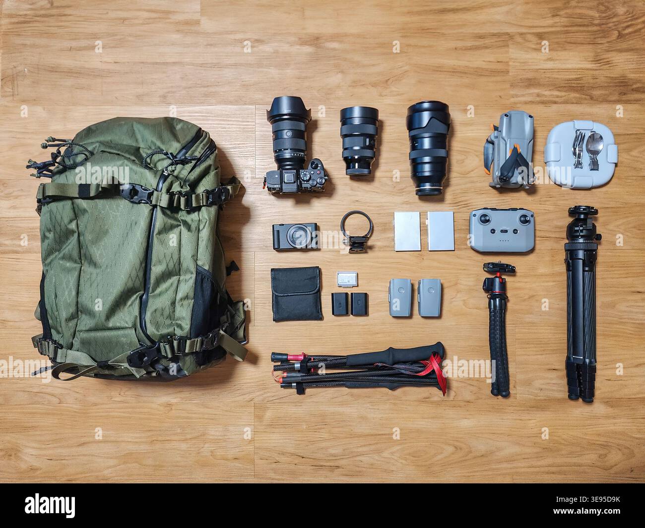 Vista dall'alto del set di moderni accessori da fotografo con fotocamera mirrorless, obiettivo, treppiede, drone e zaino su pavimento in legno Foto Stock