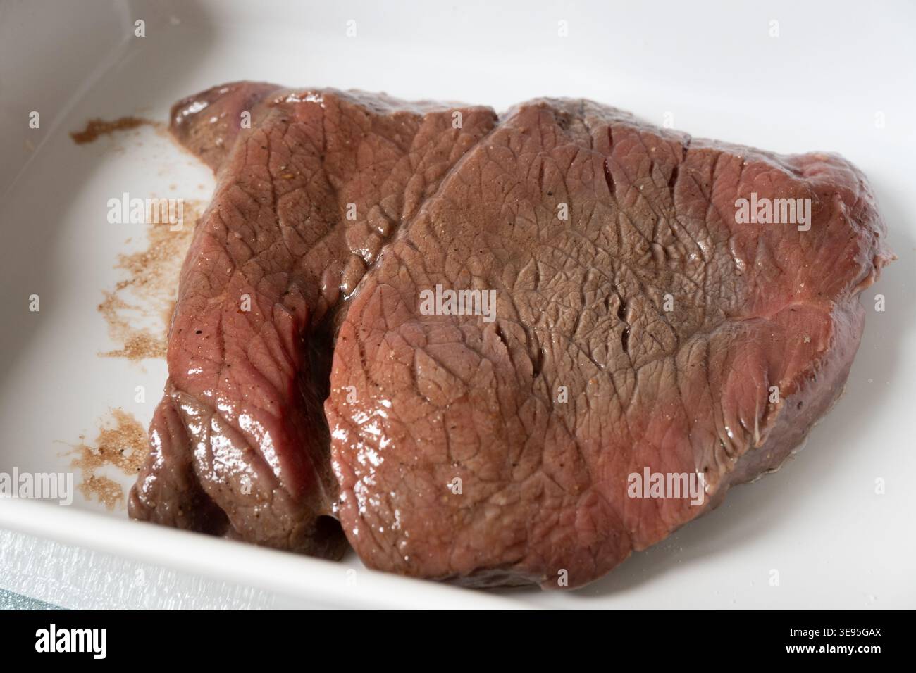 Bistecca di manzo cruda o filetto in contenitore rettangolare bianco con condimento. Perfetto per contenuti culinari, editoriali per la preparazione di alimenti e pac proteico Foto Stock