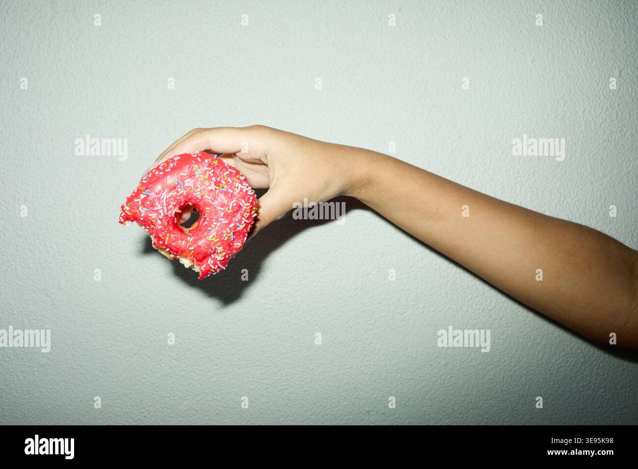 Adulto che tiene in mano Bitten Pink Donut per il concetto di bravura di snack Foto Stock