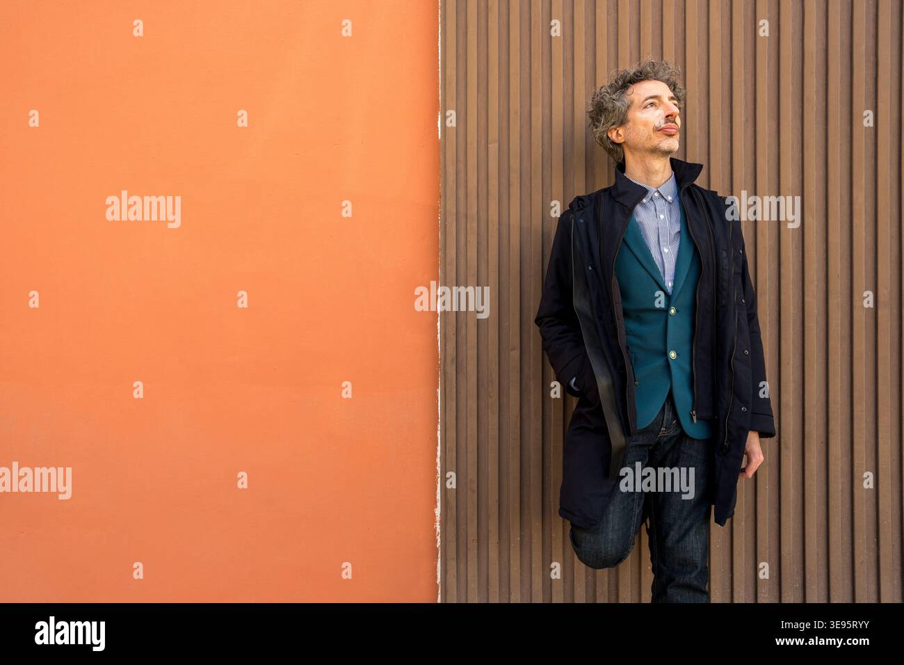Uomo con capelli ricci appoggiato a un muro testurizzato, che guarda con un'espressione premurosa, contemplando nuove idee Foto Stock