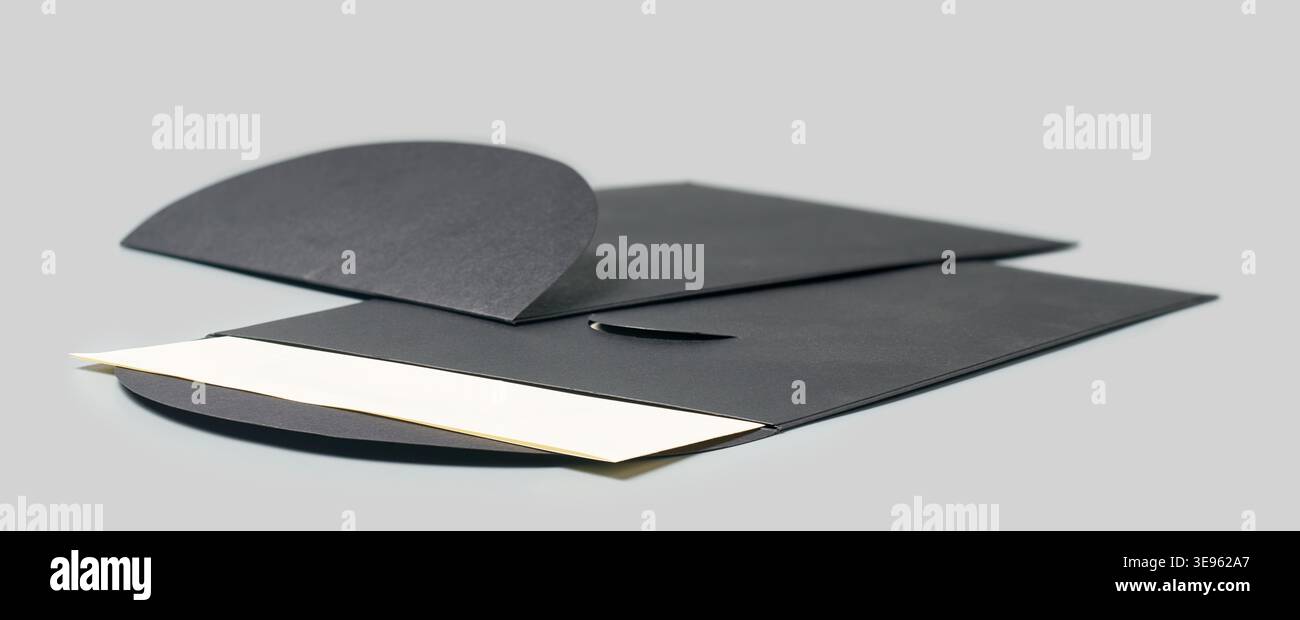 due buste di carta nera opaca con cartoncino bianco parzialmente infilato all'interno su sfondo grigio, vista laterale con messa a fuoco morbida, elegante posta di alta qualità Foto Stock
